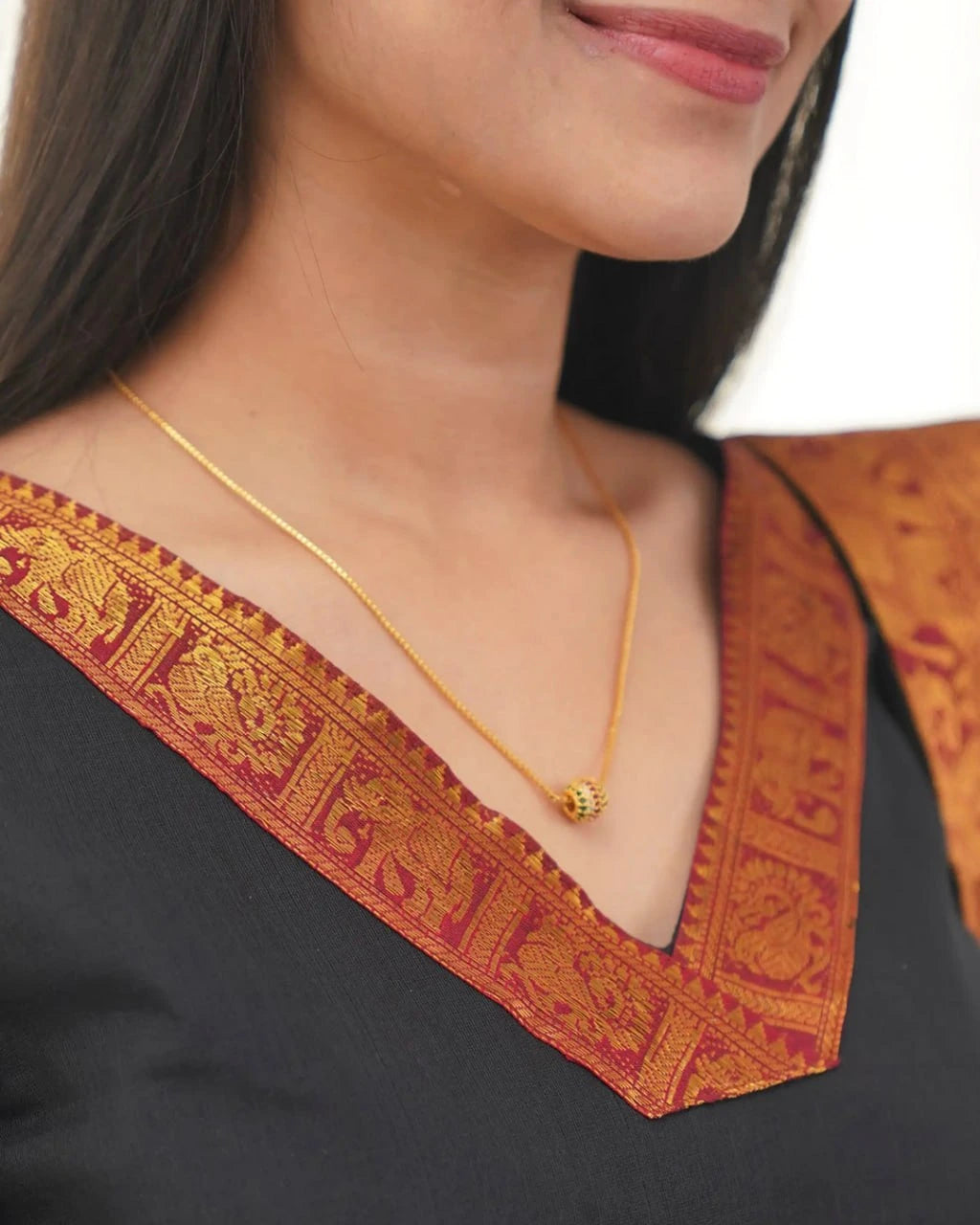 Close-up of a person wearing a gold necklace with a black and orange traditional outfit.