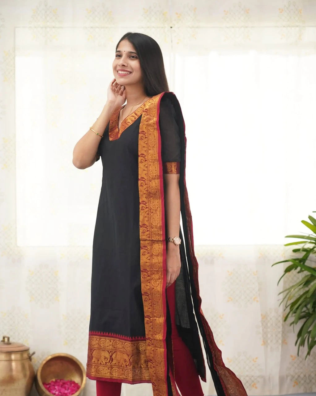 Woman wearing a black and red traditional outfit with a decorative border against a light background.