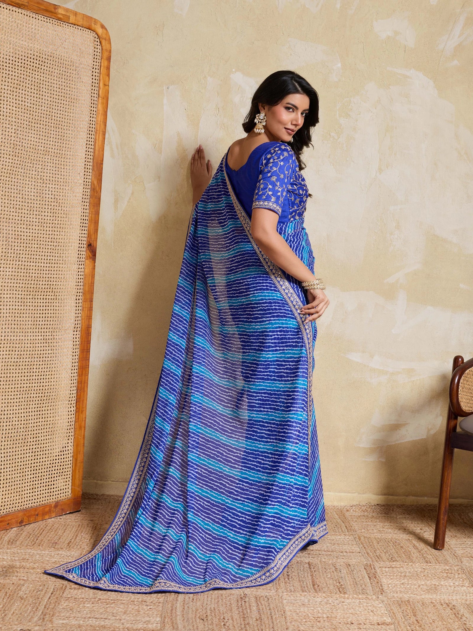 Woman wearing a blue saree with a pattern against a beige wall.