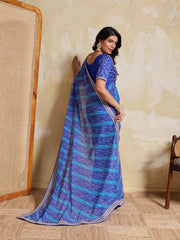 Woman wearing a blue saree with a pattern against a beige wall.