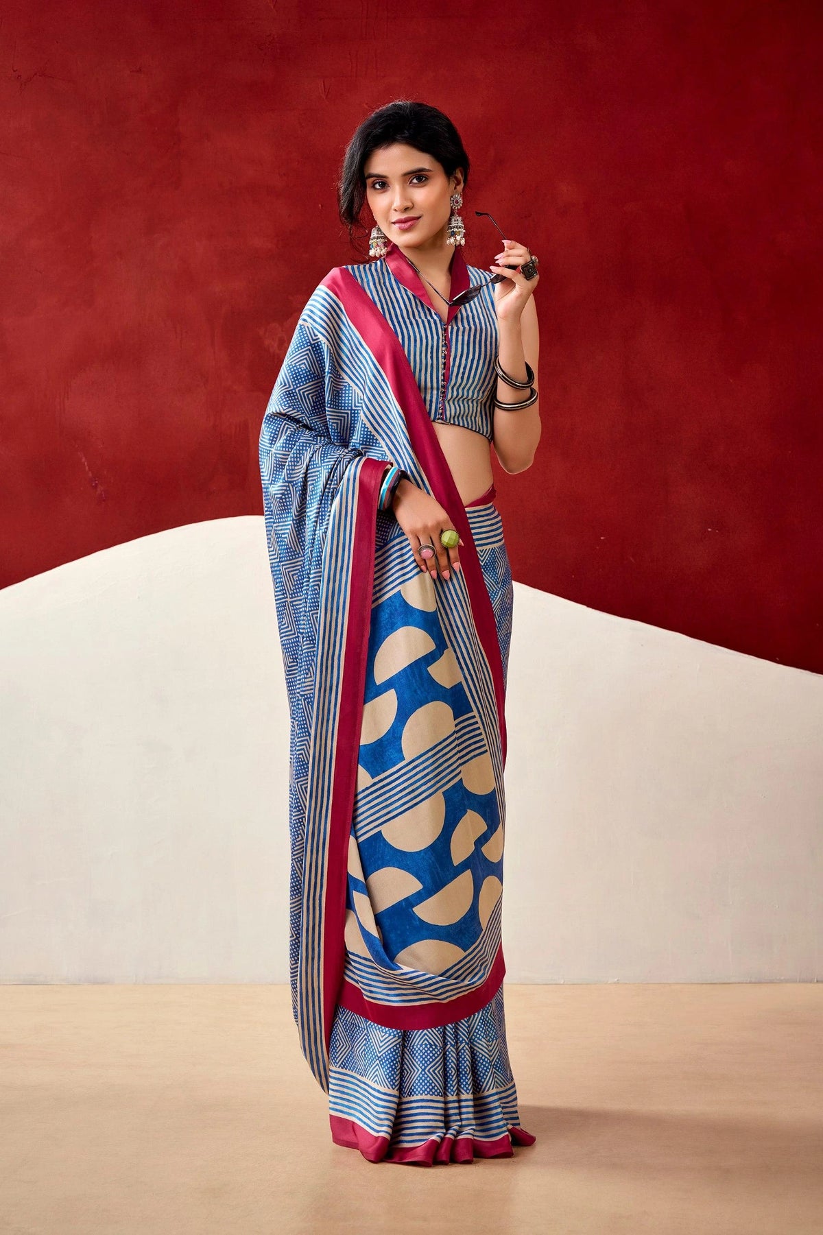 Woman wearing a blue and red saree with a patterned blouse against a red and beige background