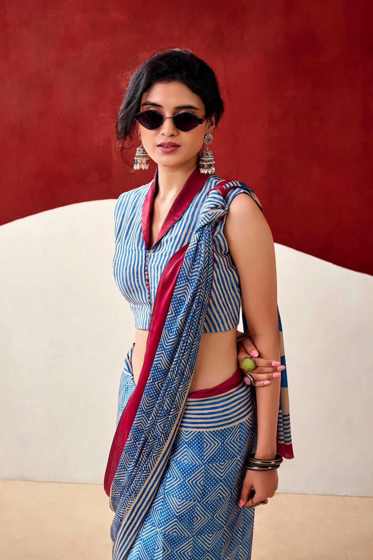 Woman wearing a blue and red saree with sunglasses against a red background