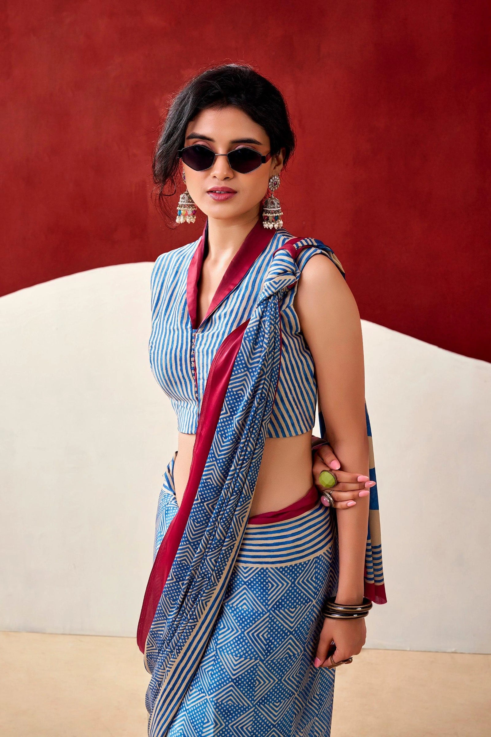 Woman wearing a blue and red saree with sunglasses against a red background
