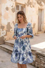 Woman wearing a blue floral dress standing in front of a textured wall.