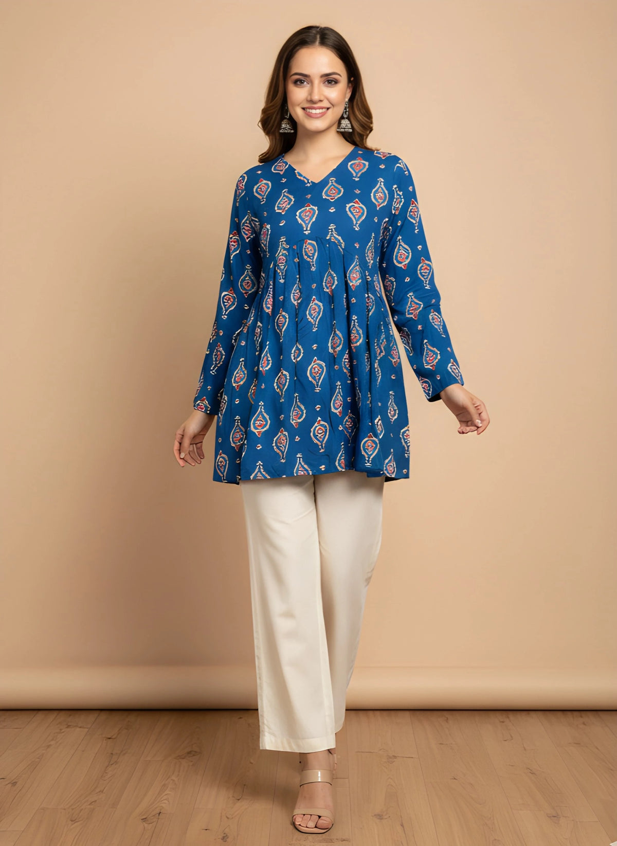 Woman wearing a blue patterned top and white pants against a beige background