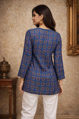Woman wearing a blue patterned top and white pants in a room with decorative elements.