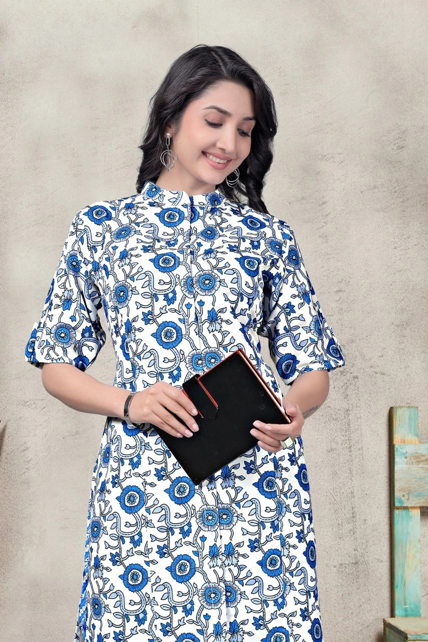 Woman wearing a blue and white floral dress holding a black book against a beige wall.