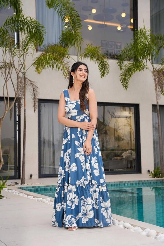 Woman in a blue floral dress standing by a pool with palm trees in the background