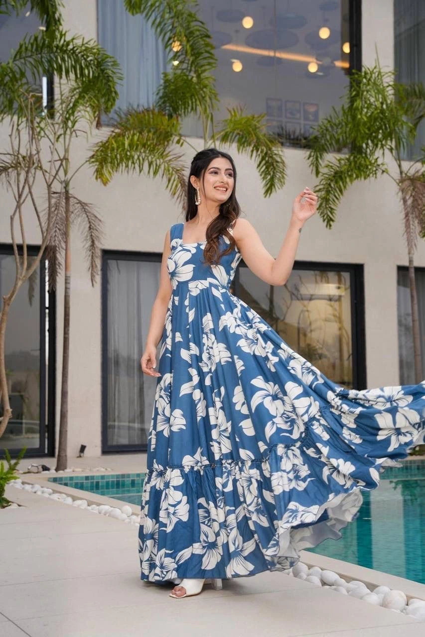 Woman in a blue floral dress standing by a pool with greenery in the background