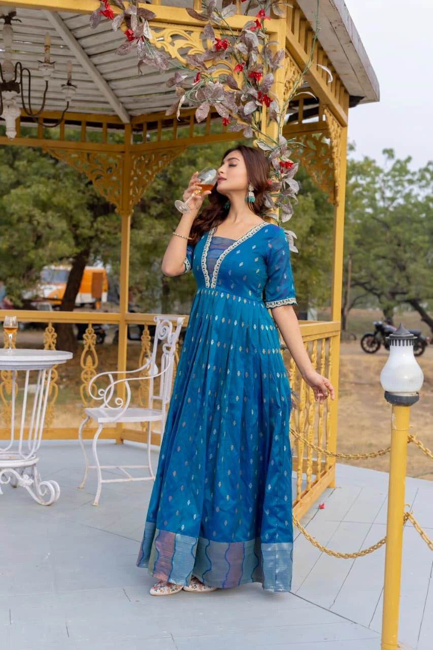 Woman in a blue dress drinking from a glass on a decorated outdoor gazebo.