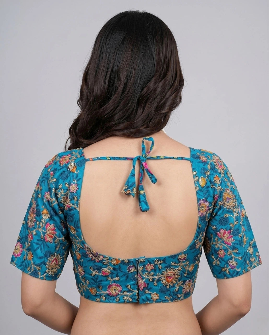 Woman wearing a blue floral blouse with an open back on a gray background