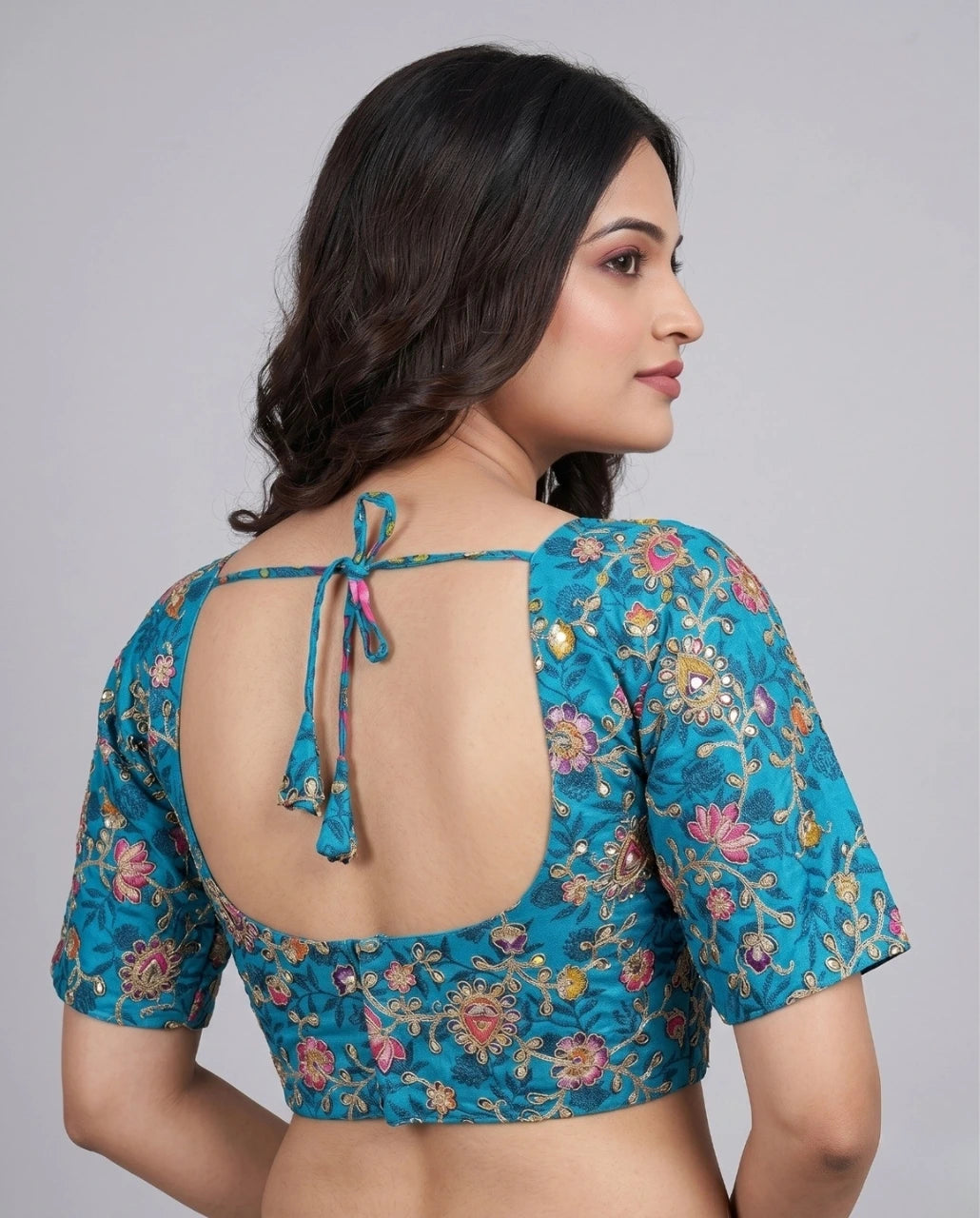 Woman wearing a blue floral blouse with an open back on a gray background