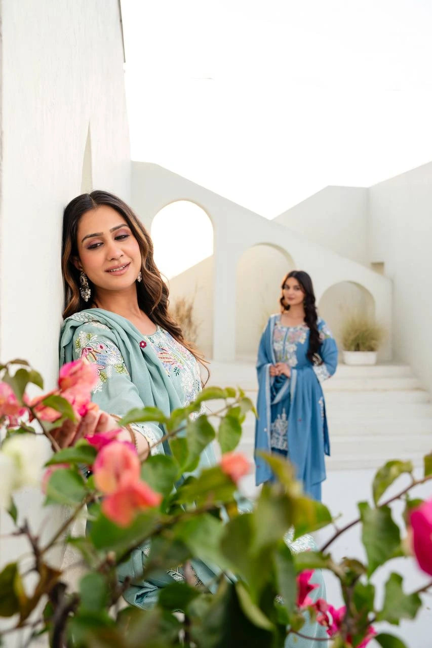 Two women in traditional attire standing in a decorative outdoor setting with flowers in the foreground.