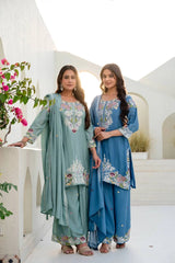 Two women in traditional embroidered outfits standing on a white architectural background.