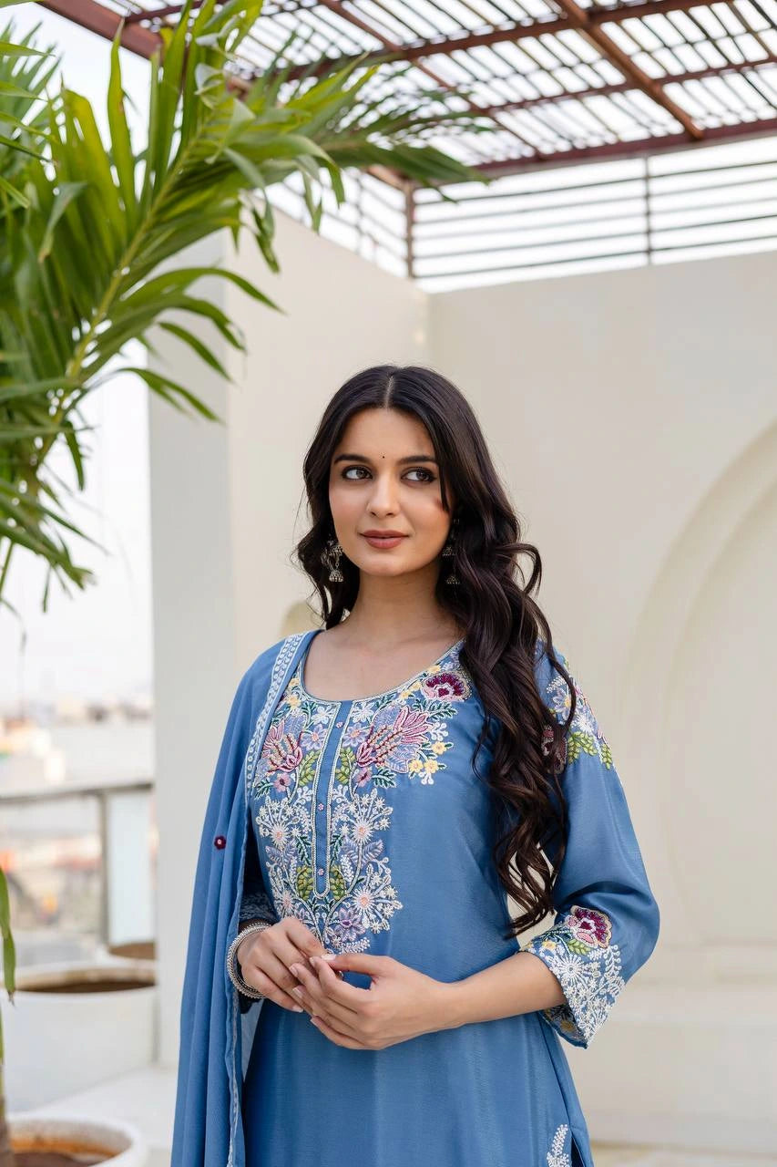 Woman wearing a blue embroidered outfit with a plant and architectural elements in the background