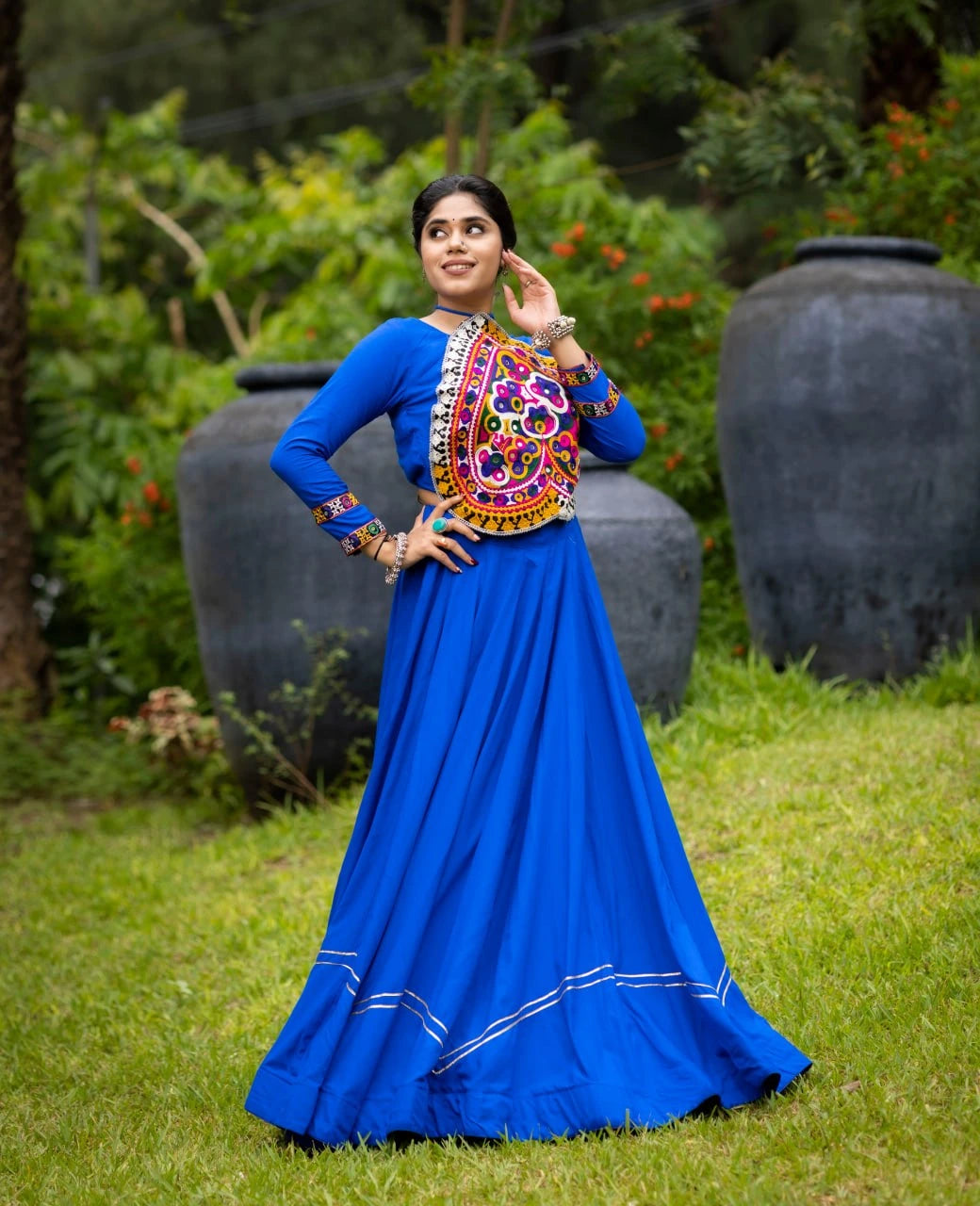 Woman in a blue traditional outfit with colorful embroidery standing outdoors.