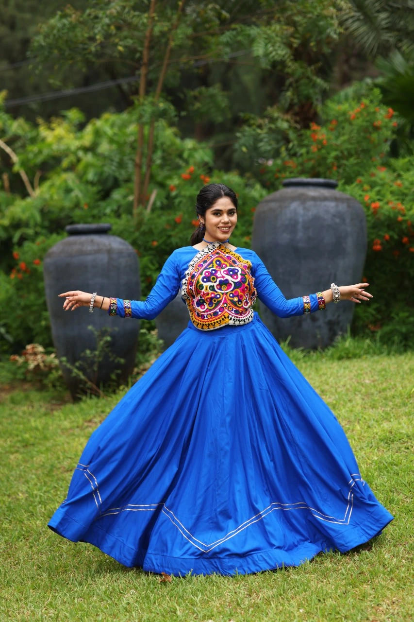 Woman in a blue traditional outfit with colorful embellishments standing outdoors.