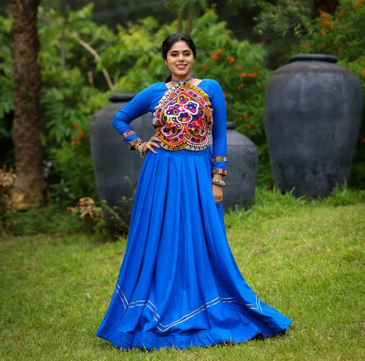 Woman in a blue traditional outfit with colorful embroidery standing outdoors.