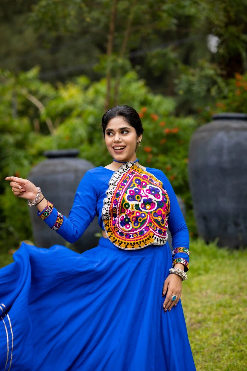Woman in a blue traditional outfit with colorful embroidery dancing outdoors.