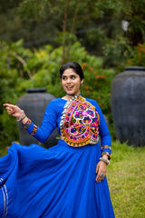 Woman in a blue traditional outfit with colorful embroidery dancing outdoors.