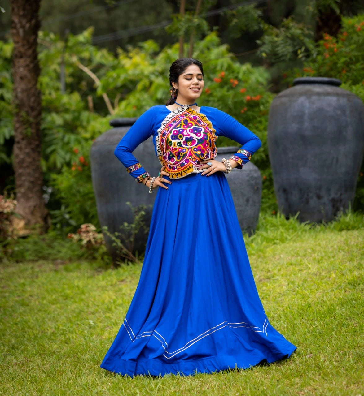 Woman in a colorful traditional outfit standing outdoors with greenery in the background