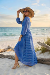 Woman in a blue dress and sun hat standing on a beach with ocean view
