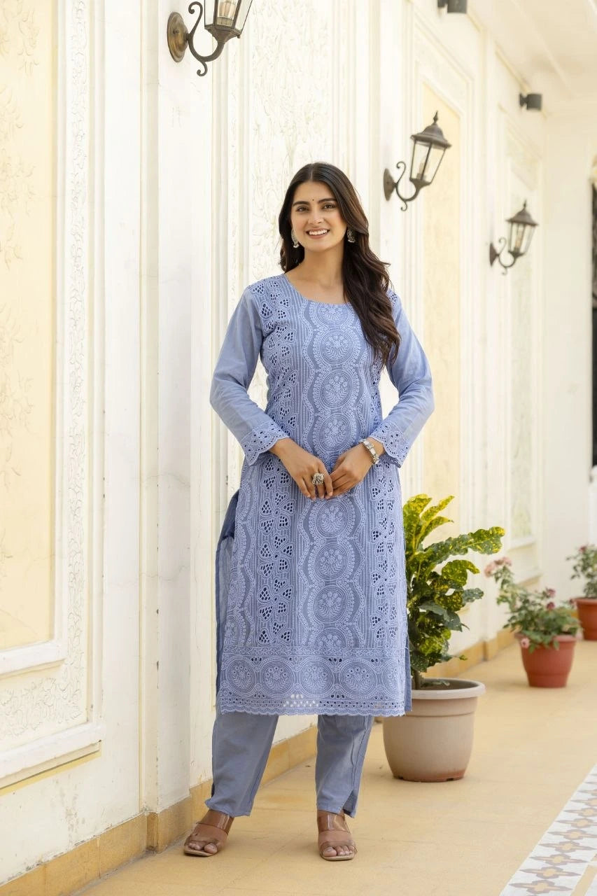 Woman wearing a blue embroidered kurta with pants standing in a decorative outdoor setting.