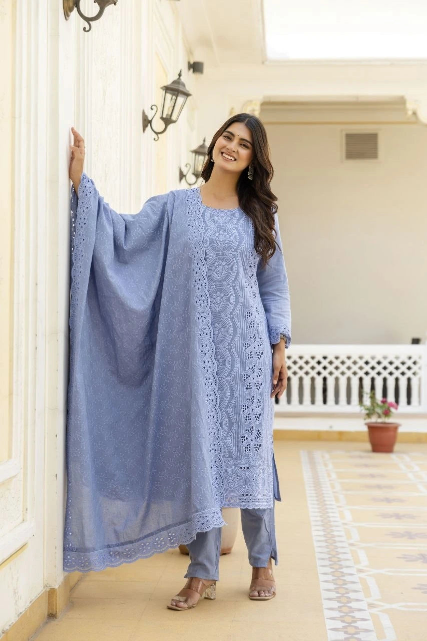 Woman in a blue embroidered outfit standing in a well-lit room with white walls and a decorative rug.