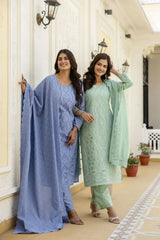 Two women in matching blue and green traditional outfits standing in a decorative indoor setting.