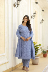 Woman wearing a blue embroidered outfit standing in a decorative hallway.