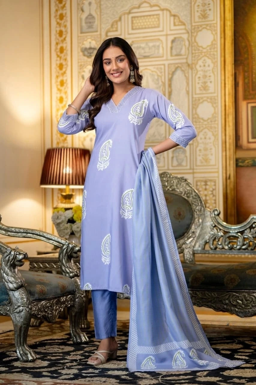Woman in a light blue traditional outfit with white patterns standing in an ornate room.