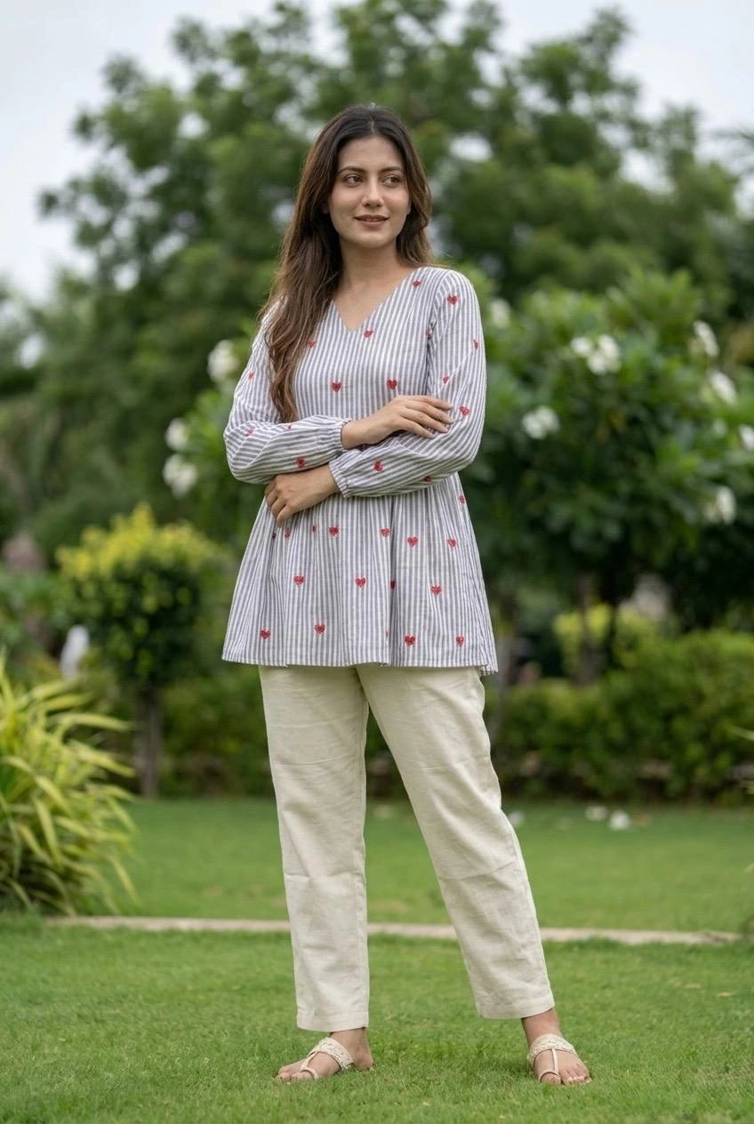 Woman wearing a striped shirt with floral patterns and beige pants standing in a garden.