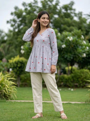 Woman wearing a checkered top with red patterns and beige pants in a garden setting
