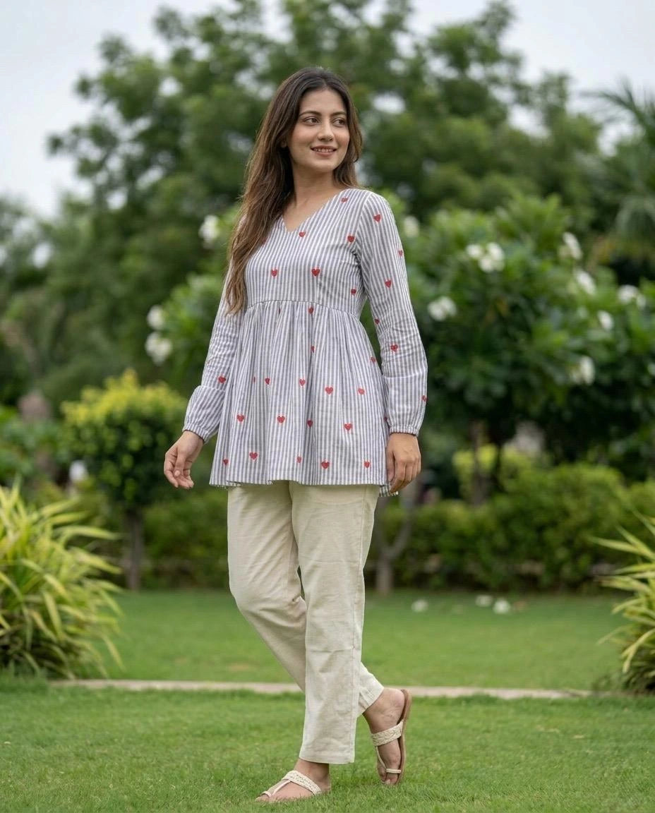 Woman wearing a checkered top with red patterns and beige pants in a garden setting