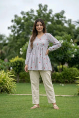 Woman wearing a white checkered top and beige pants standing in a garden.