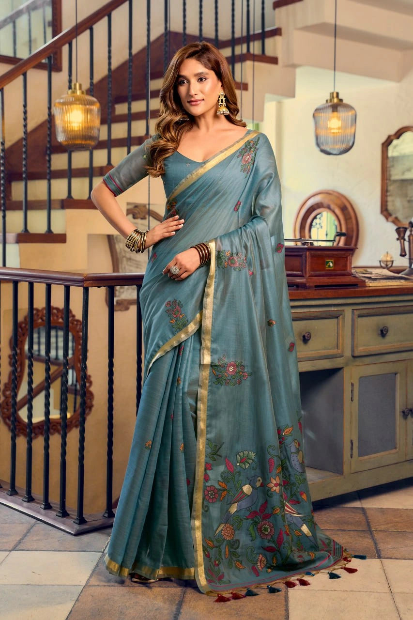 Woman in a blue saree with floral patterns standing in an indoor setting.