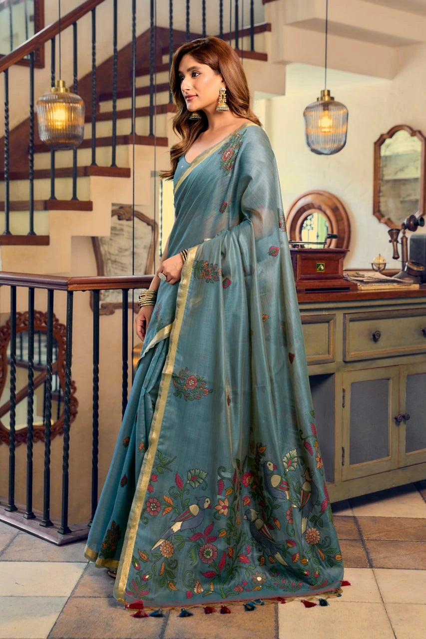 Woman wearing a blue saree with floral patterns in an indoor setting.