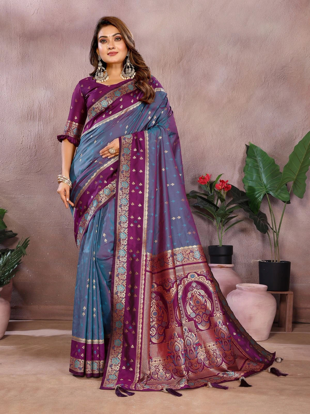 Woman wearing a blue and purple saree with a patterned border, standing against a neutral background.