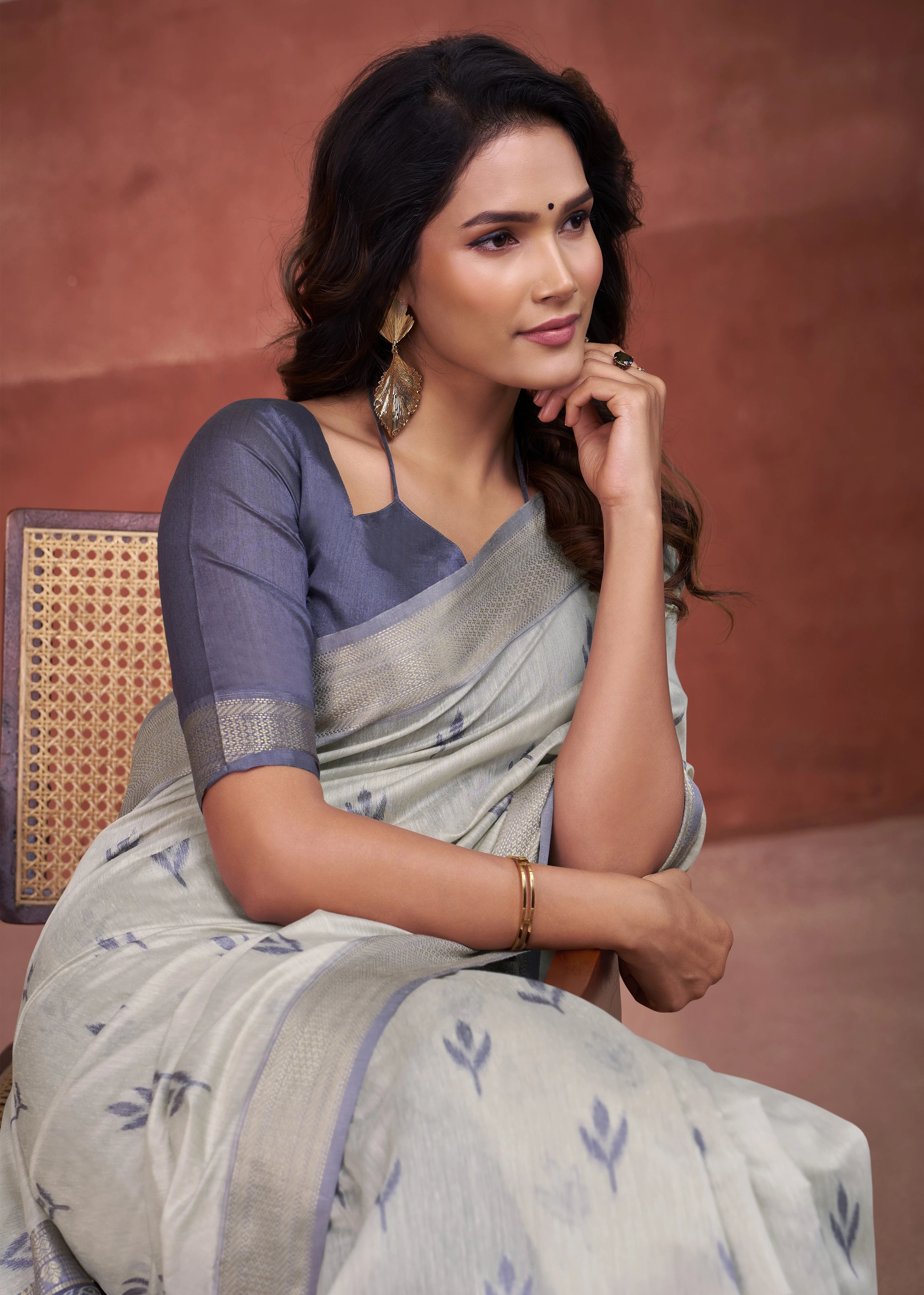 Woman in a saree sitting on a chair with a brown background