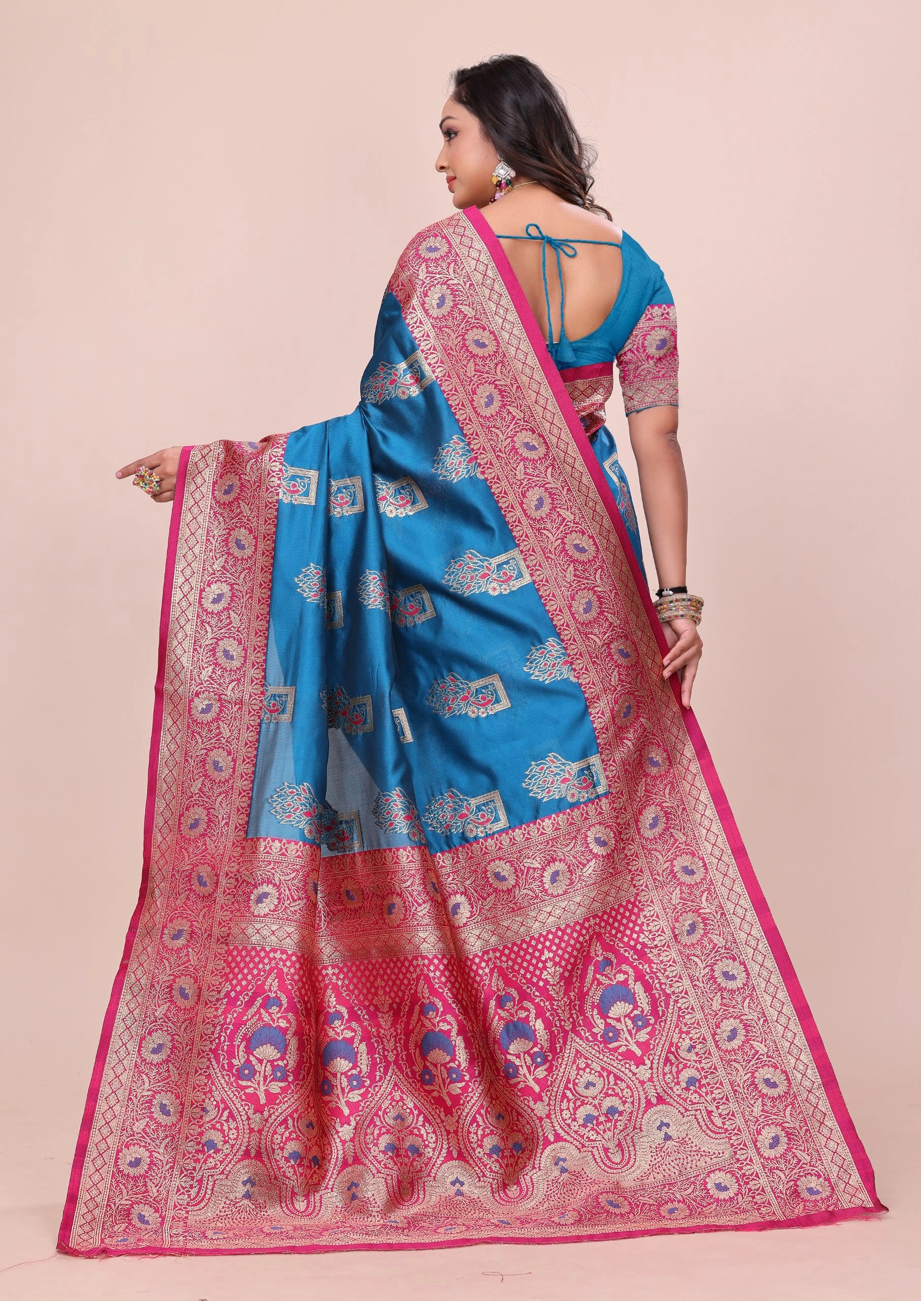 Woman wearing a pink and blue saree with intricate patterns on a beige background