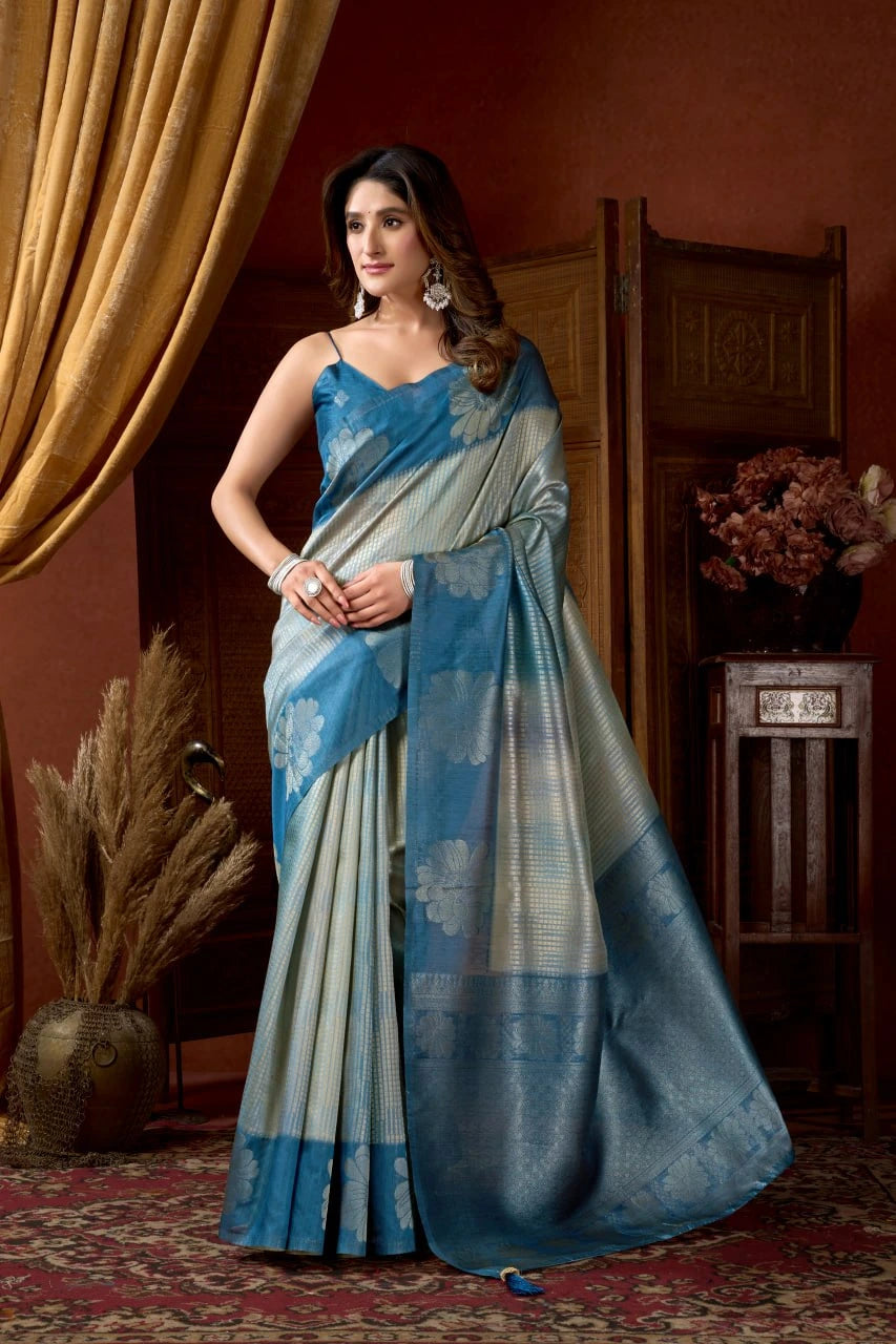 Woman wearing a blue and gray saree in an indoor setting with decorative elements.