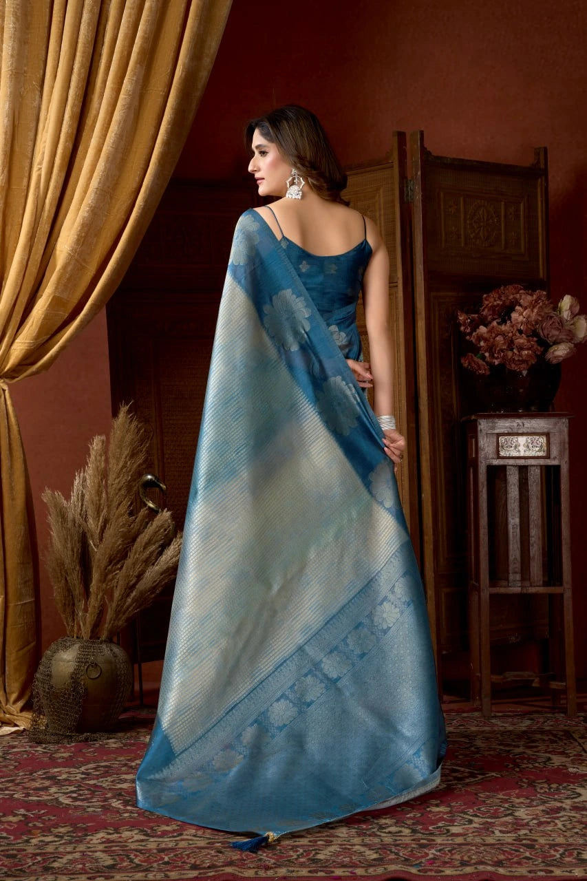 Woman in a blue saree standing in a room with decorative elements.