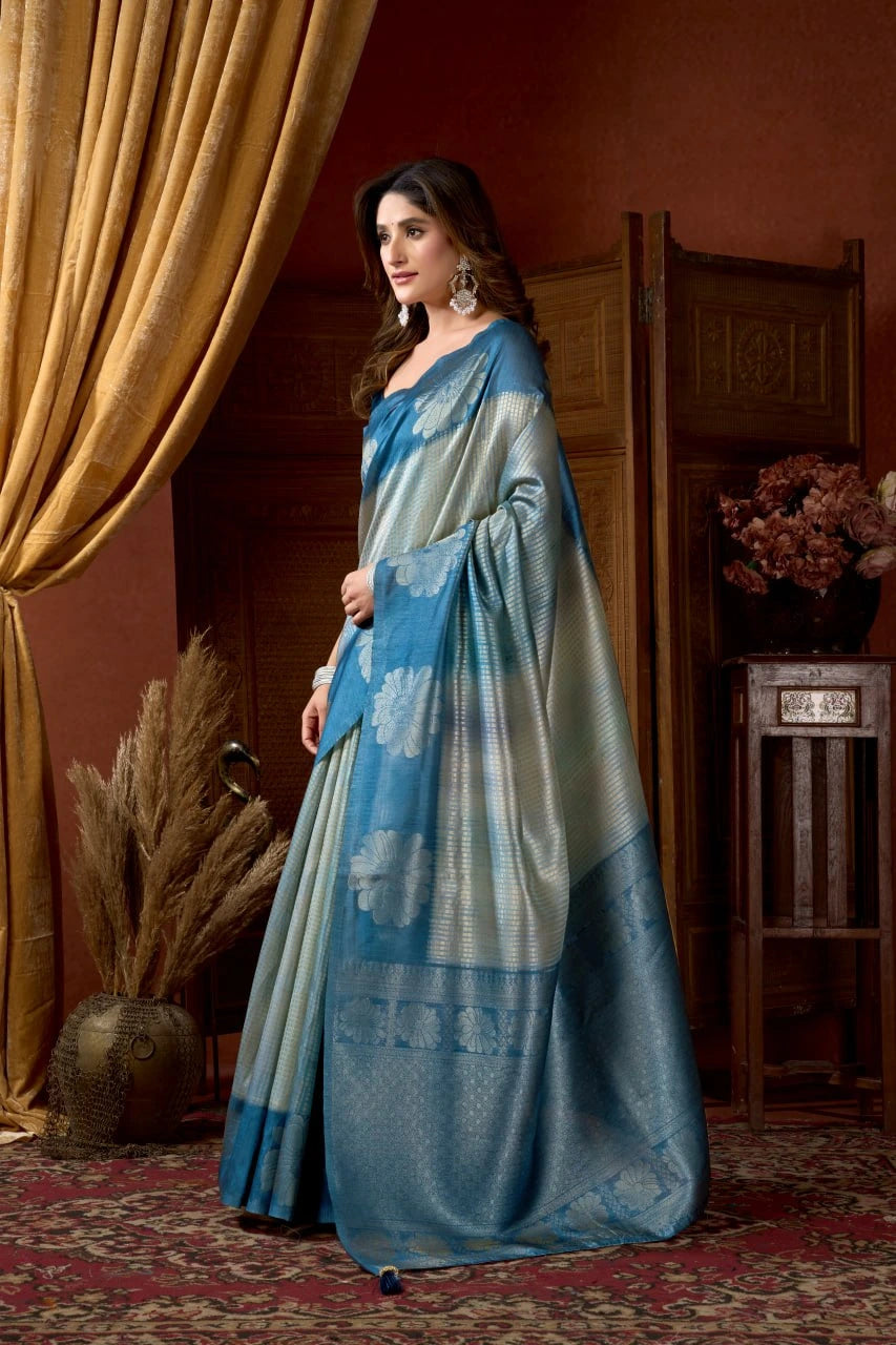 Woman in a blue and white saree standing in a room with decorative elements.