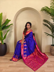 Woman in a blue and pink saree sitting indoors with plants around