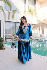 Woman in a blue traditional outfit standing by a pool with modern building and plants in the background