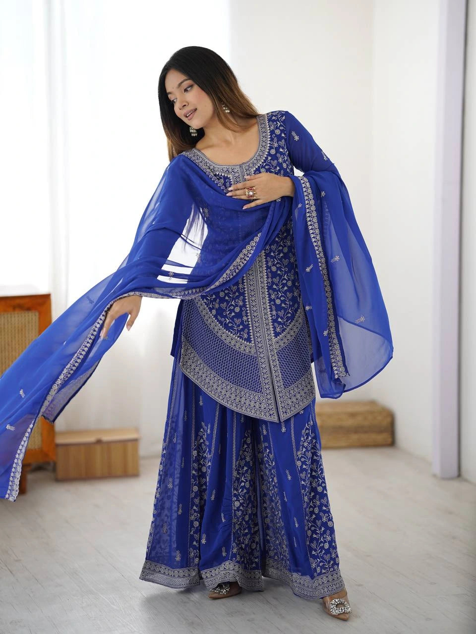 Woman wearing a blue traditional outfit with a matching dupatta in a minimal indoor setting.