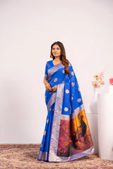 Woman wearing a blue saree with a scenic design, standing against a white background.
