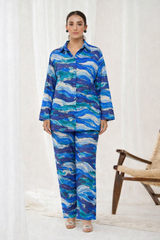 Woman wearing a blue and green patterned outfit standing in front of a white curtain.