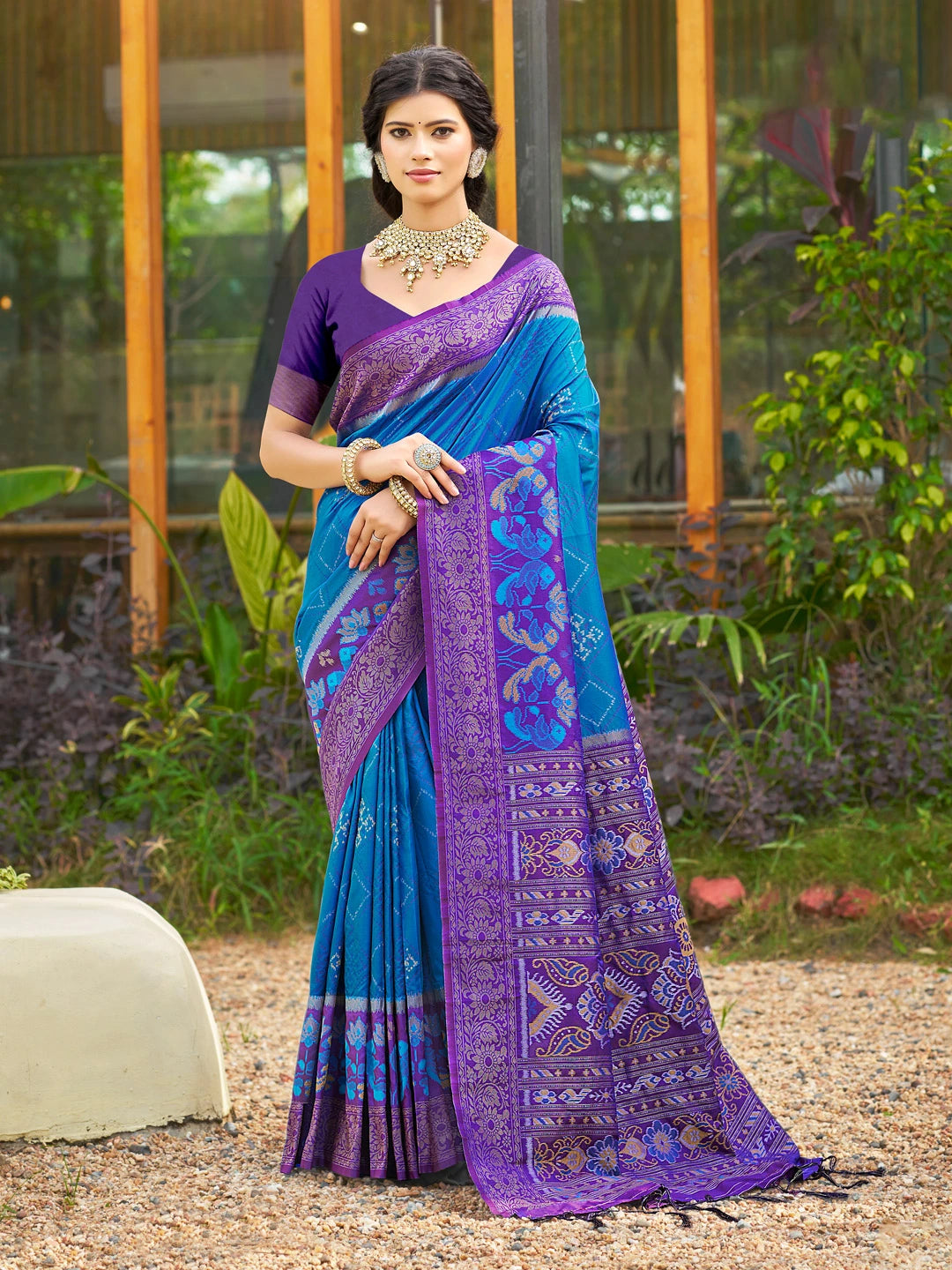 Woman wearing a blue and purple saree with a garden background