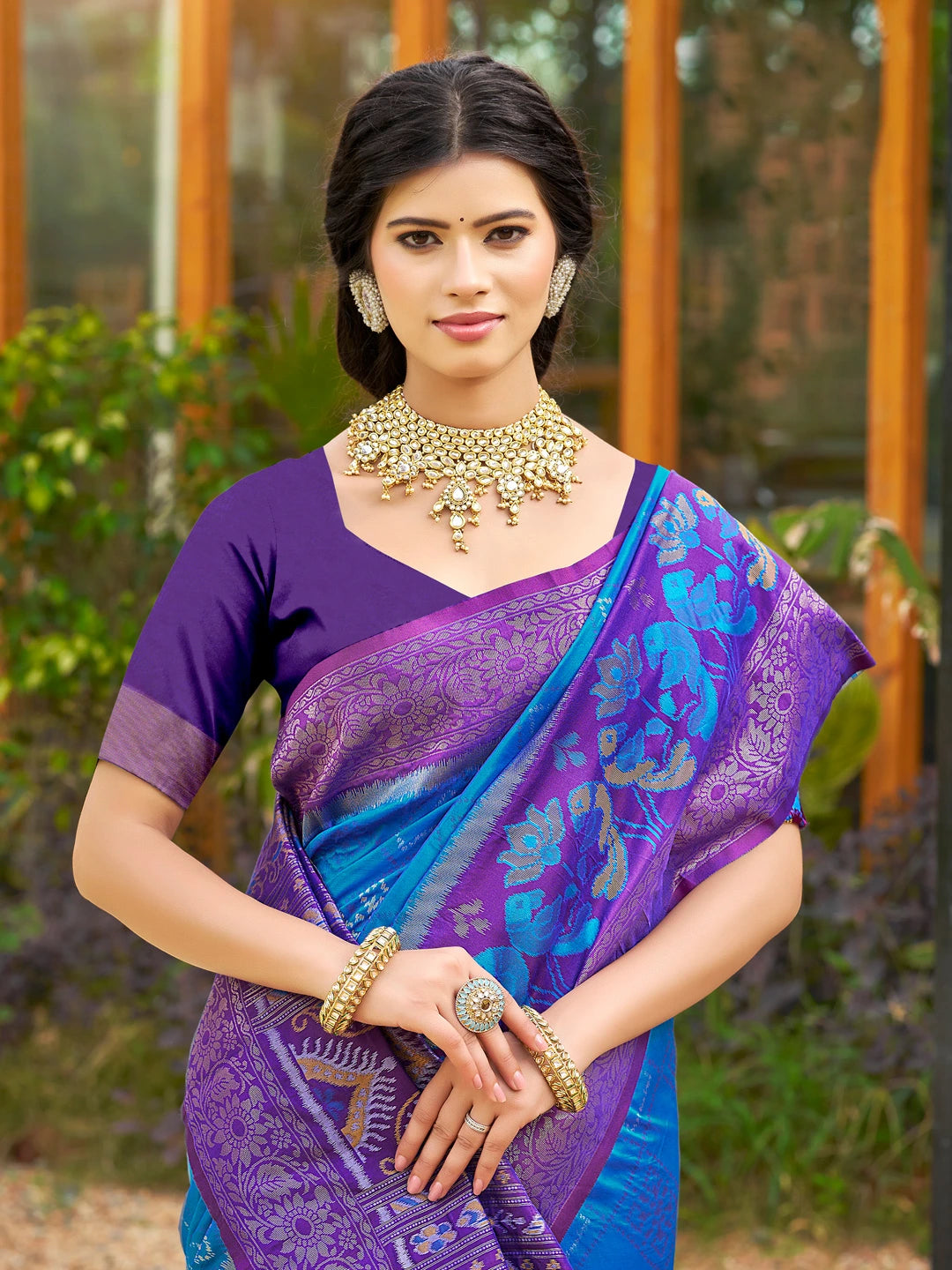 Woman wearing a purple saree with a blue blouse, standing outdoors.